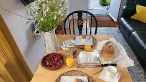 Un desayuno con huevos, tostadas y un bol de fruta sobre una mesa de madera.