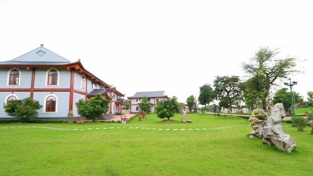 A traditional building with a red and white facade, surrounded by a well-maintained lawn and trees. - Resort Huu Bang (Hai Phong)