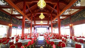 A banquet hall with red chairs and round tables, a wooden ceiling with chandeliers, and murals on the walls. - Resort Huu Bang (Hai Phong)