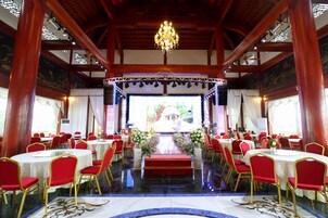 Un salón de banquetes con mesas redondas, sillas rojas y un escenario central con alfombra roja.
