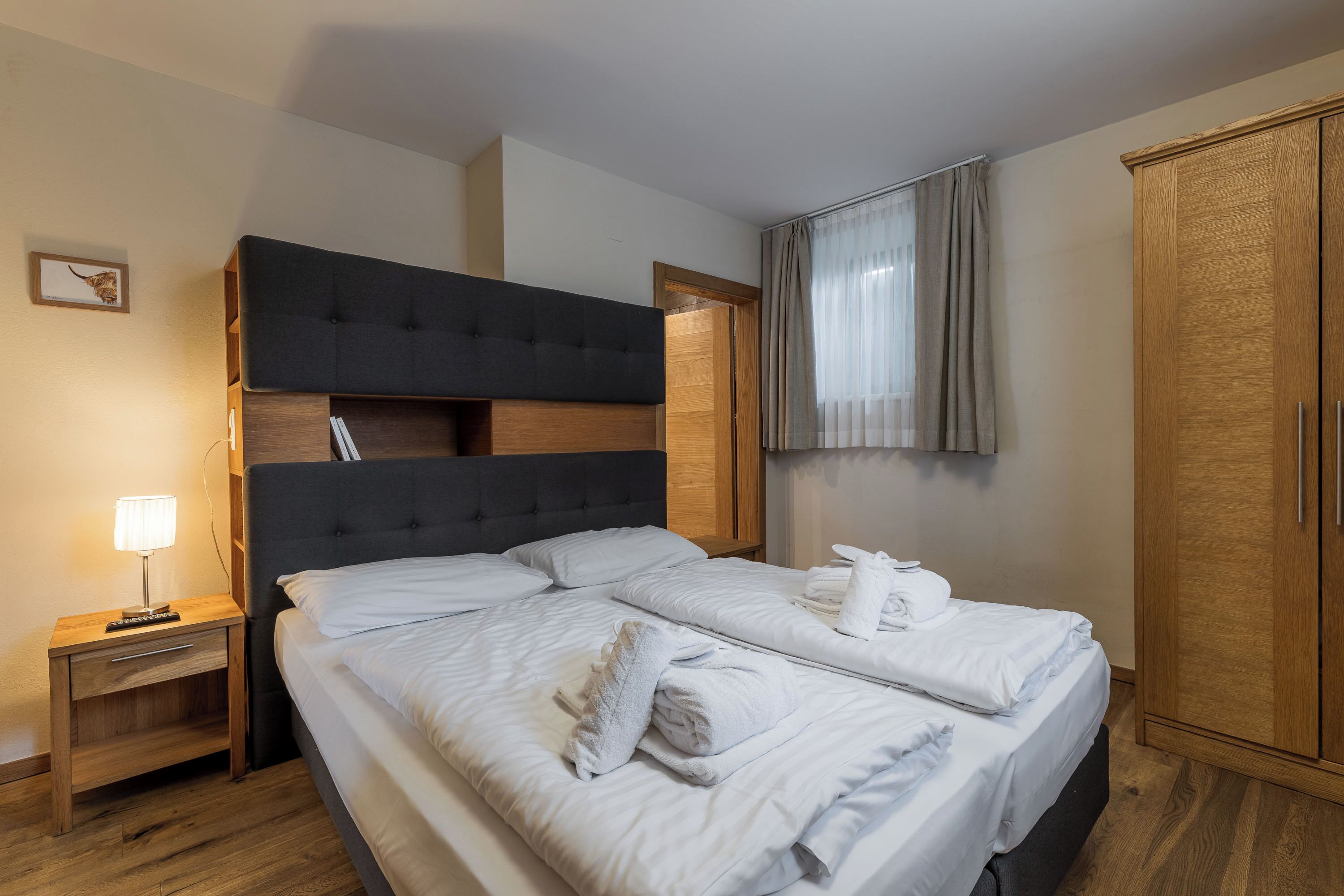 A hotel room with a large bed, a bedside table with a lamp, a wardrobe, and a framed picture on the wall.