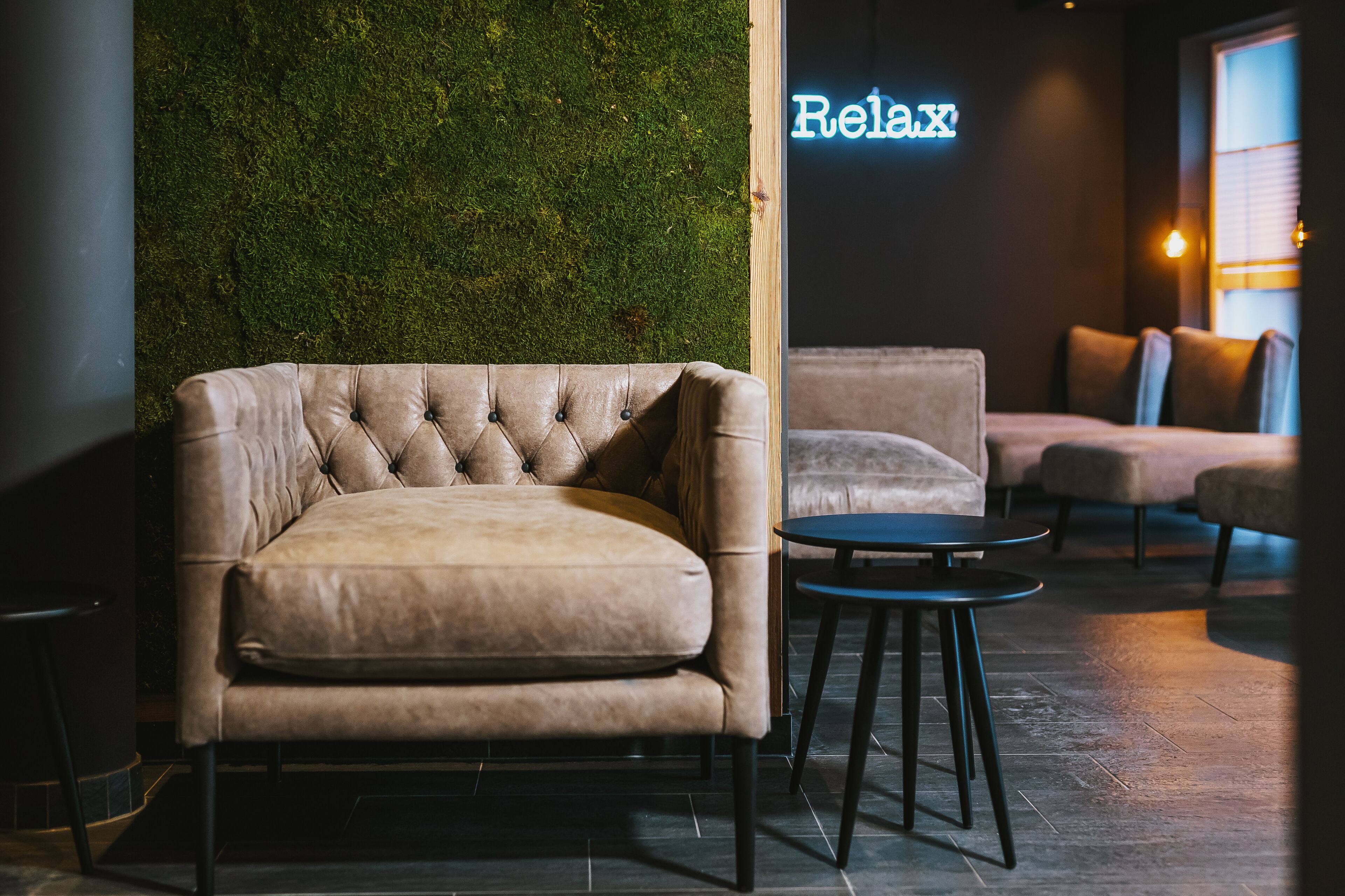 A modern lounge area with a tufted leather sofa, a round table, and a green moss wall.