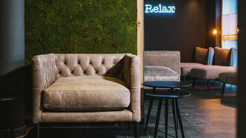 A modern lounge area with a tufted leather sofa, a round table, and a green moss wall.