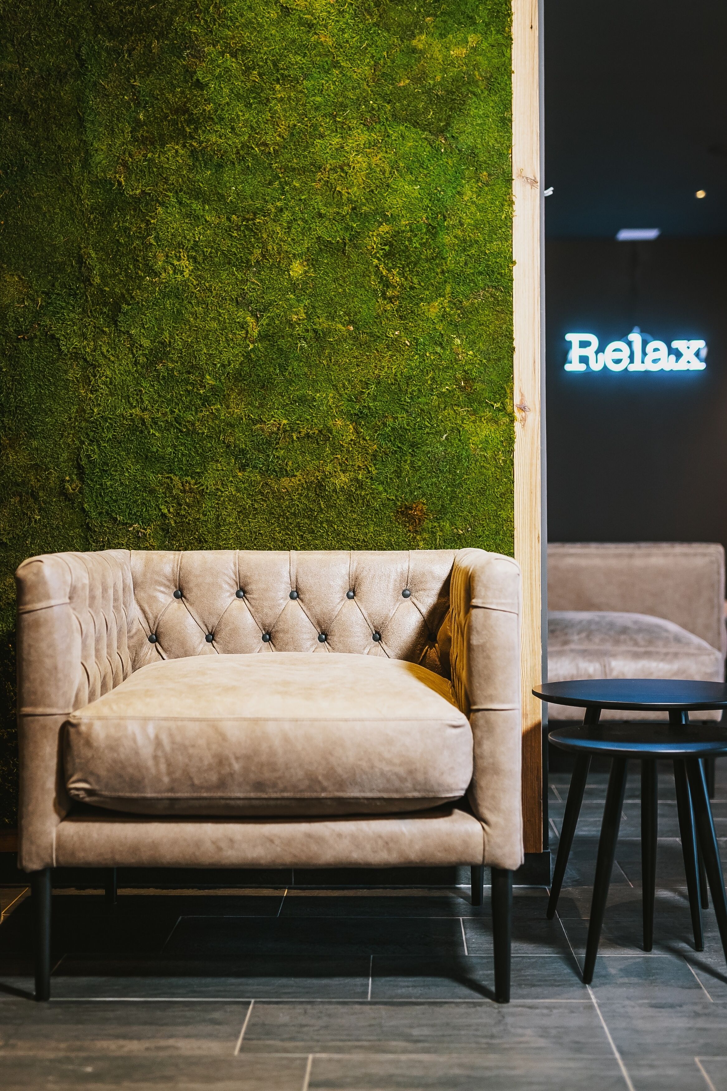 A beige tufted sofa in a modern room with a green moss wall and a neon sign that reads "Relax".