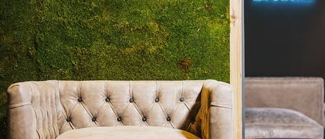 A beige tufted sofa in a modern room with a green moss wall and a neon sign that reads "Relax".