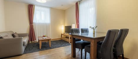 A modern living room with a sofa, a dining table with chairs, a TV, and a lamp.