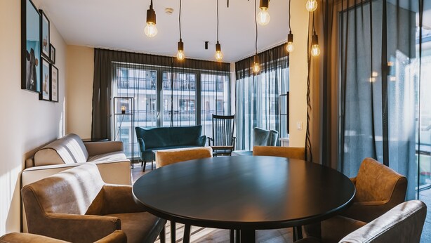 Een moderne vergaderruimte met een ronde tafel, comfortabele zitplaatsen en grote ramen voorzien van gordijnen.