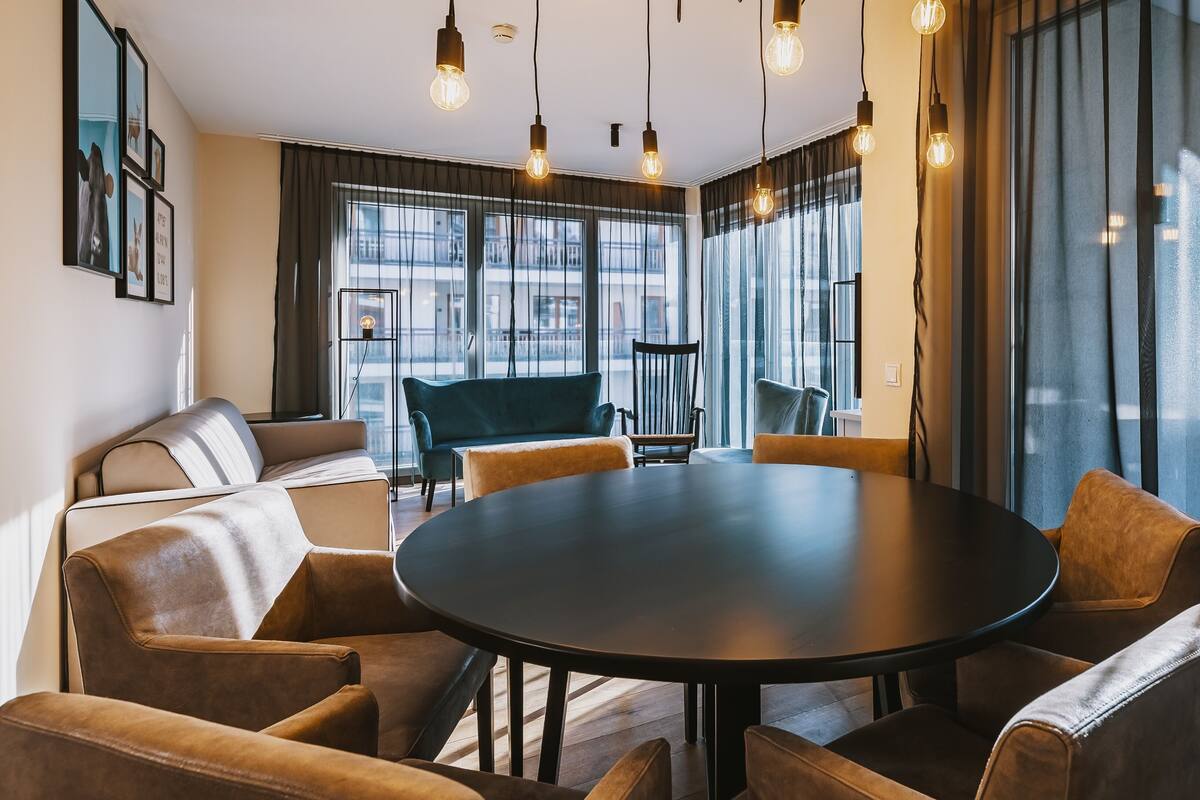 A modern meeting room with a round table, comfortable seating, and large windows with curtains.