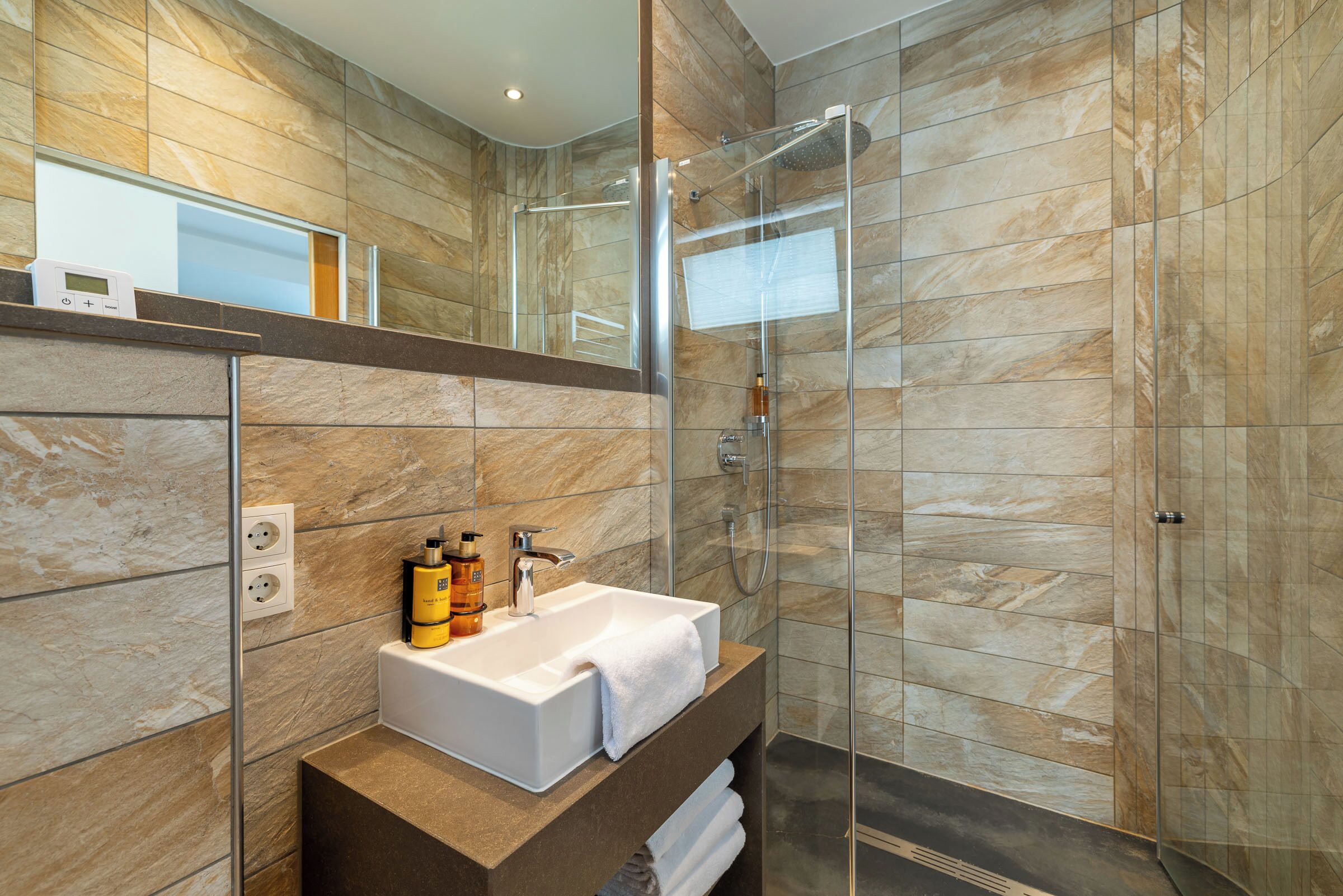 Un baño moderno con cabina de ducha de vidrio, un lavamanos blanco y un revestimiento de pared de mármol.