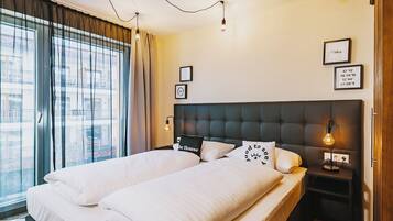 A hotel room with a large bed, two bedside tables, and a view of the city through floor-to-ceiling windows.
