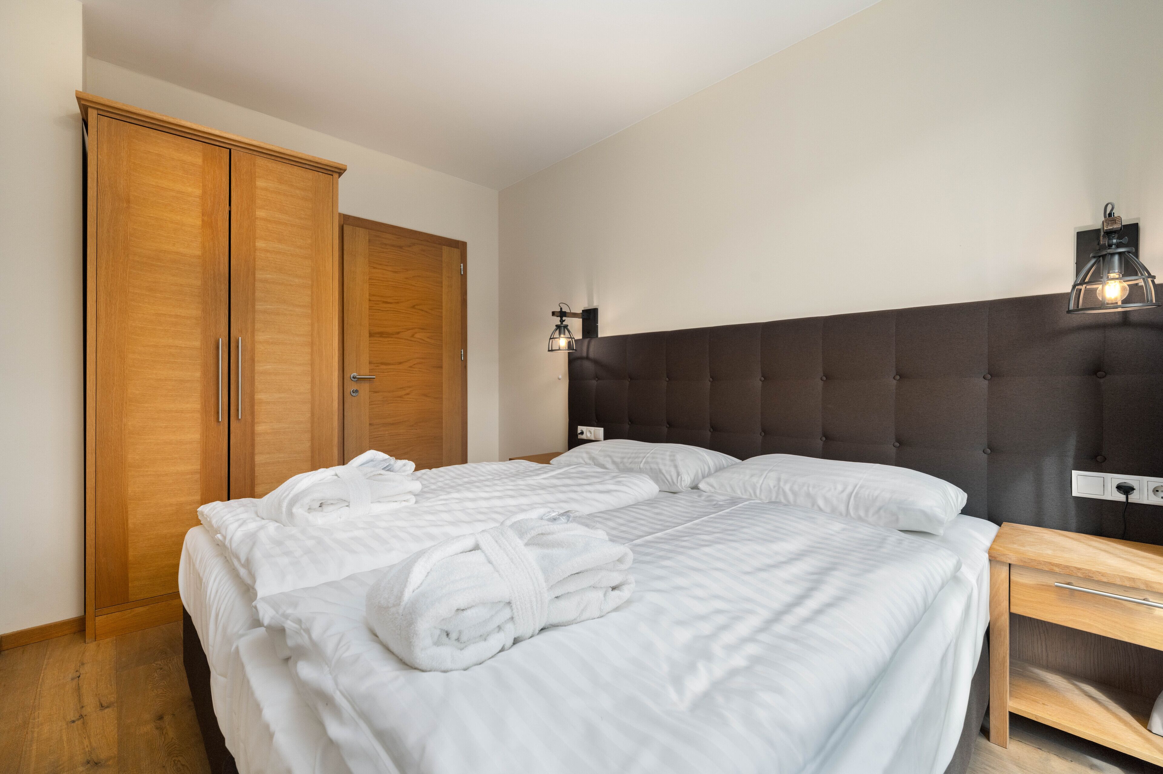 A bedroom with a large bed, two wooden wardrobes, a bedside table, and a wall-mounted light fixture.