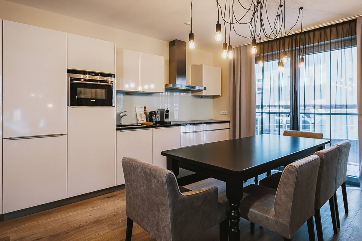 A modern kitchen with white cabinets, a black dining table, and a view of the city through large windows.
