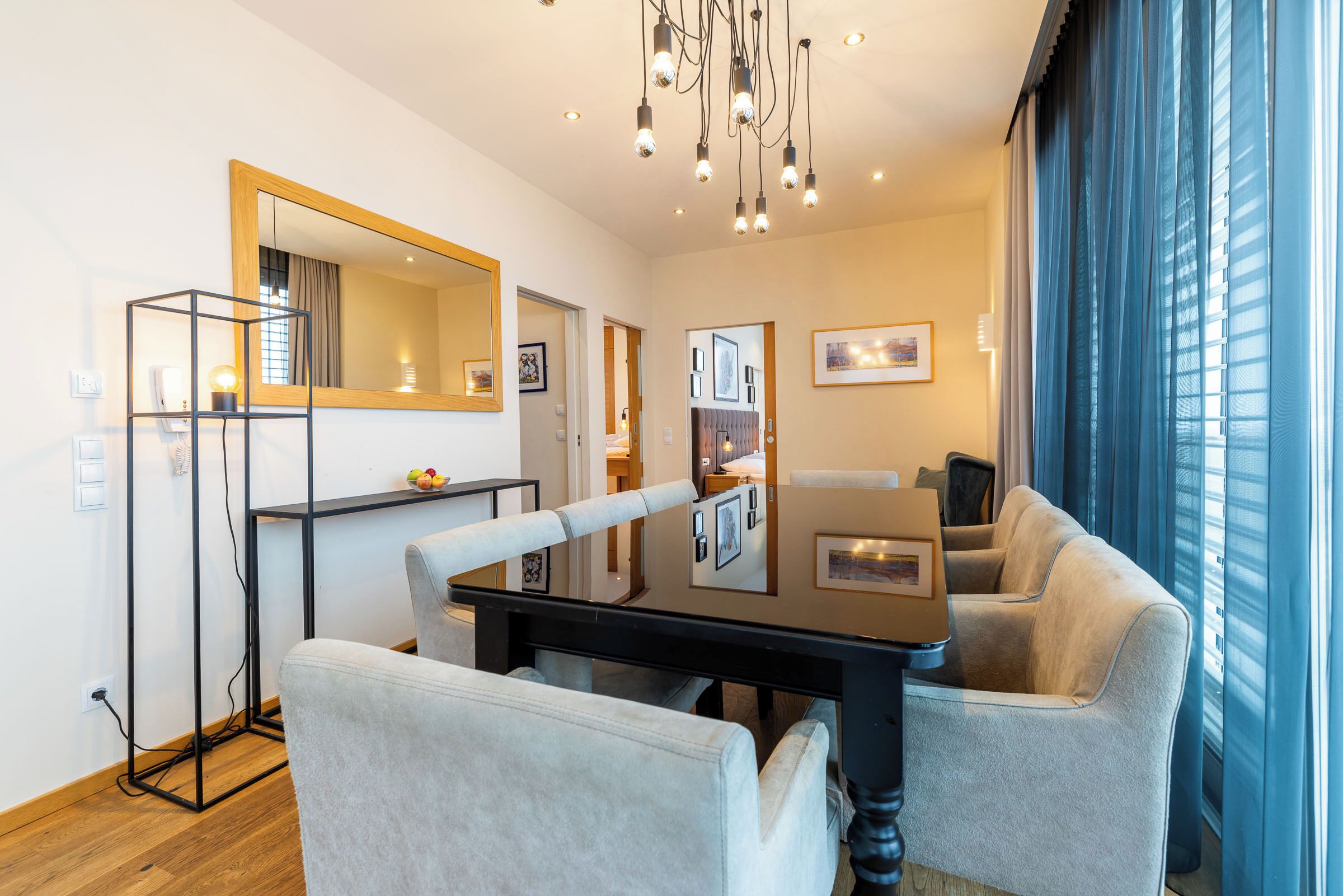 A modern living room with a dining table, two sofas, a large mirror, and a chandelier.