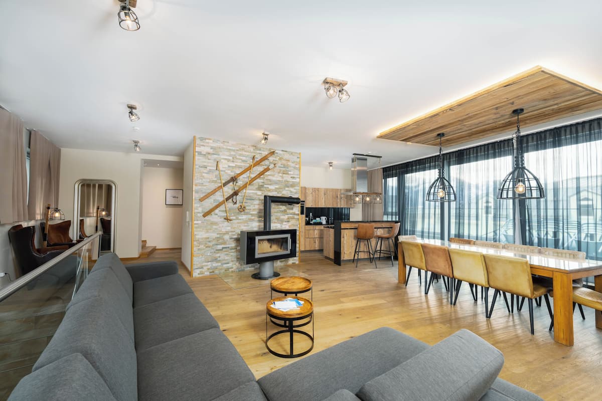 A modern living room with a grey sofa, wooden dining table, and a kitchen area with a stove.