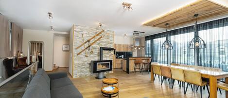 A modern living room with a grey sofa, wooden dining table, and a kitchen area with a stove.