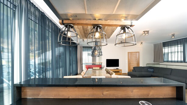 A modern kitchen with a large island, pendant lighting, and a view of the living area. - The House Zell am See (Zell am See)