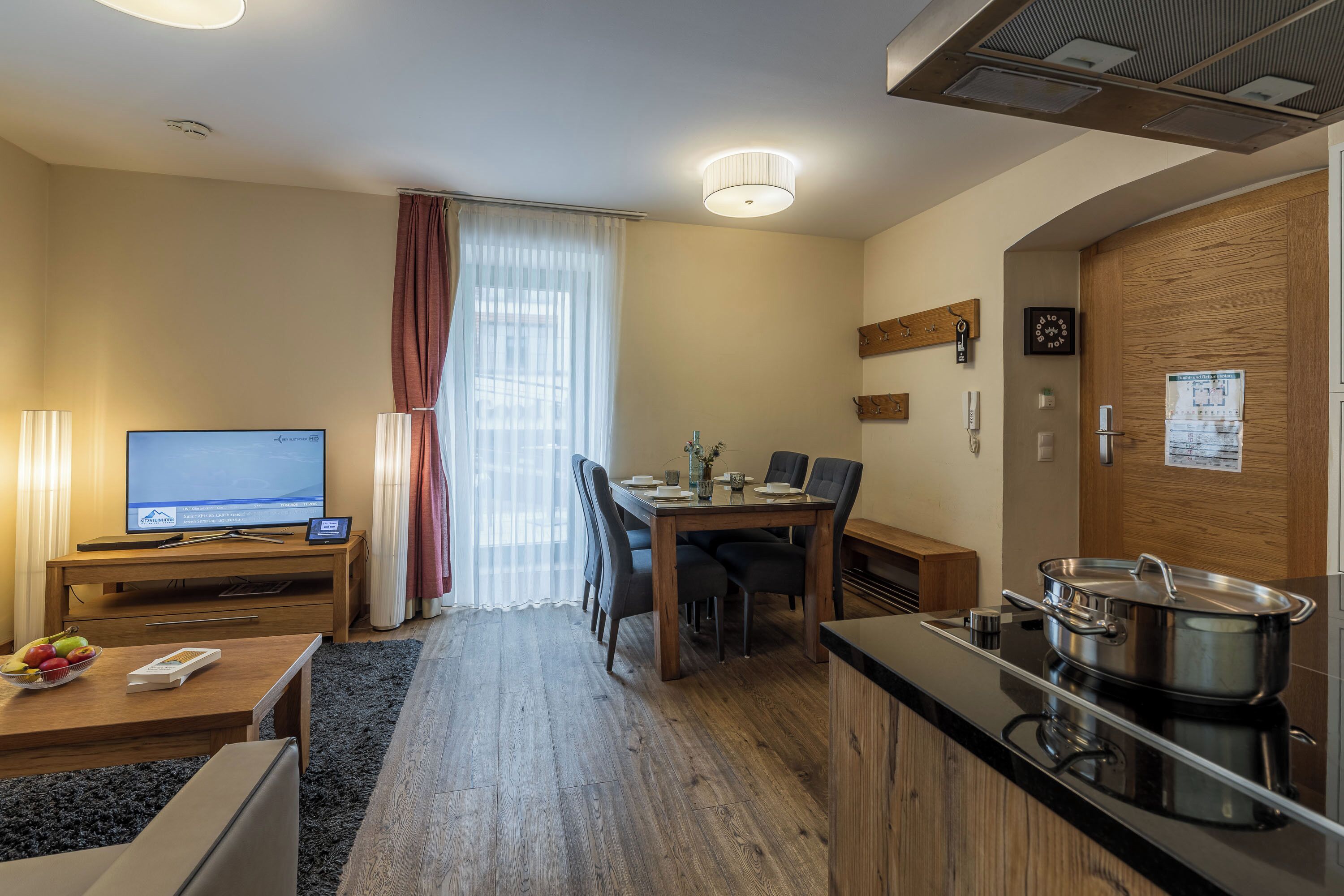 A compact hotel room with a dining area, a TV, a kitchenette, and a wooden door.