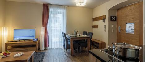 A compact hotel room with a dining area, a TV, a kitchenette, and a wooden door.