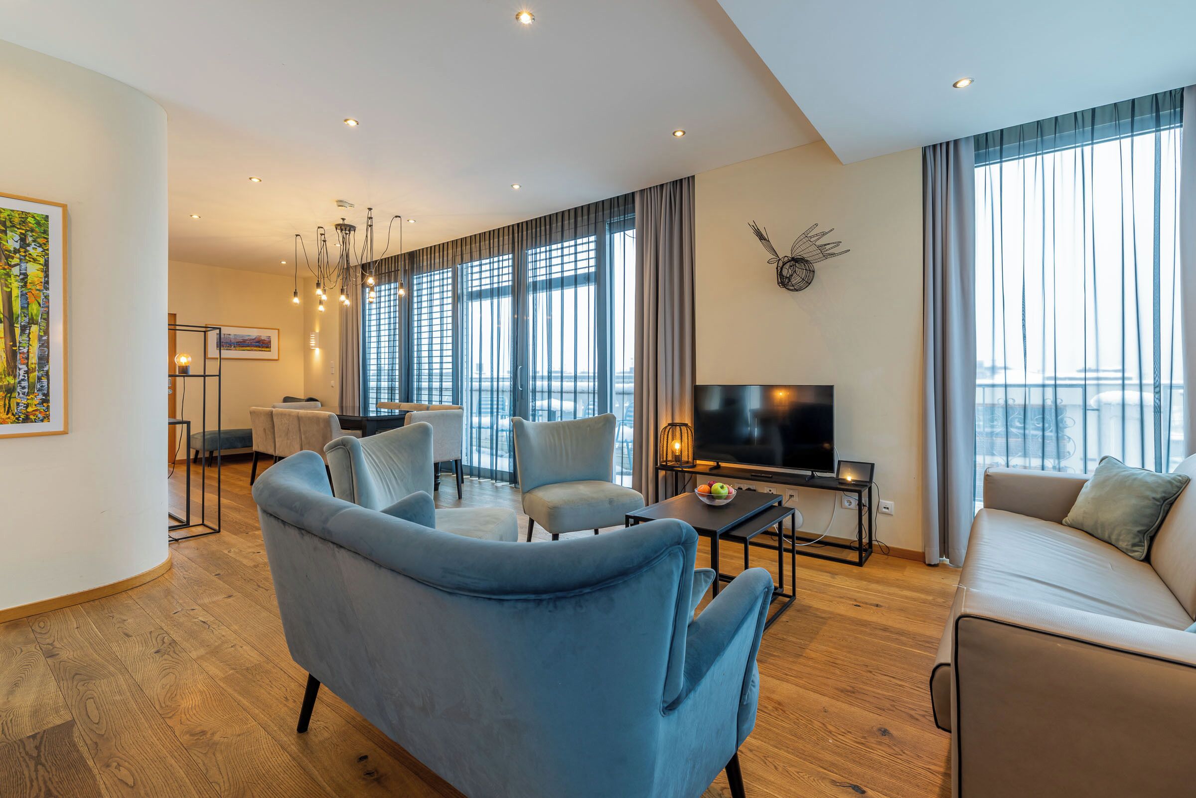 A modern living room with a sofa, armchairs, a TV, and a dining area with a table and chairs.