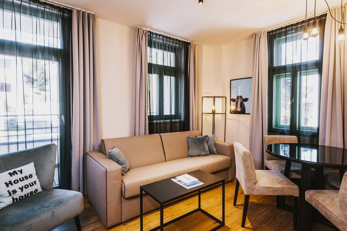 A modern living room with a sofa, armchairs, a coffee table, and a dining table.
