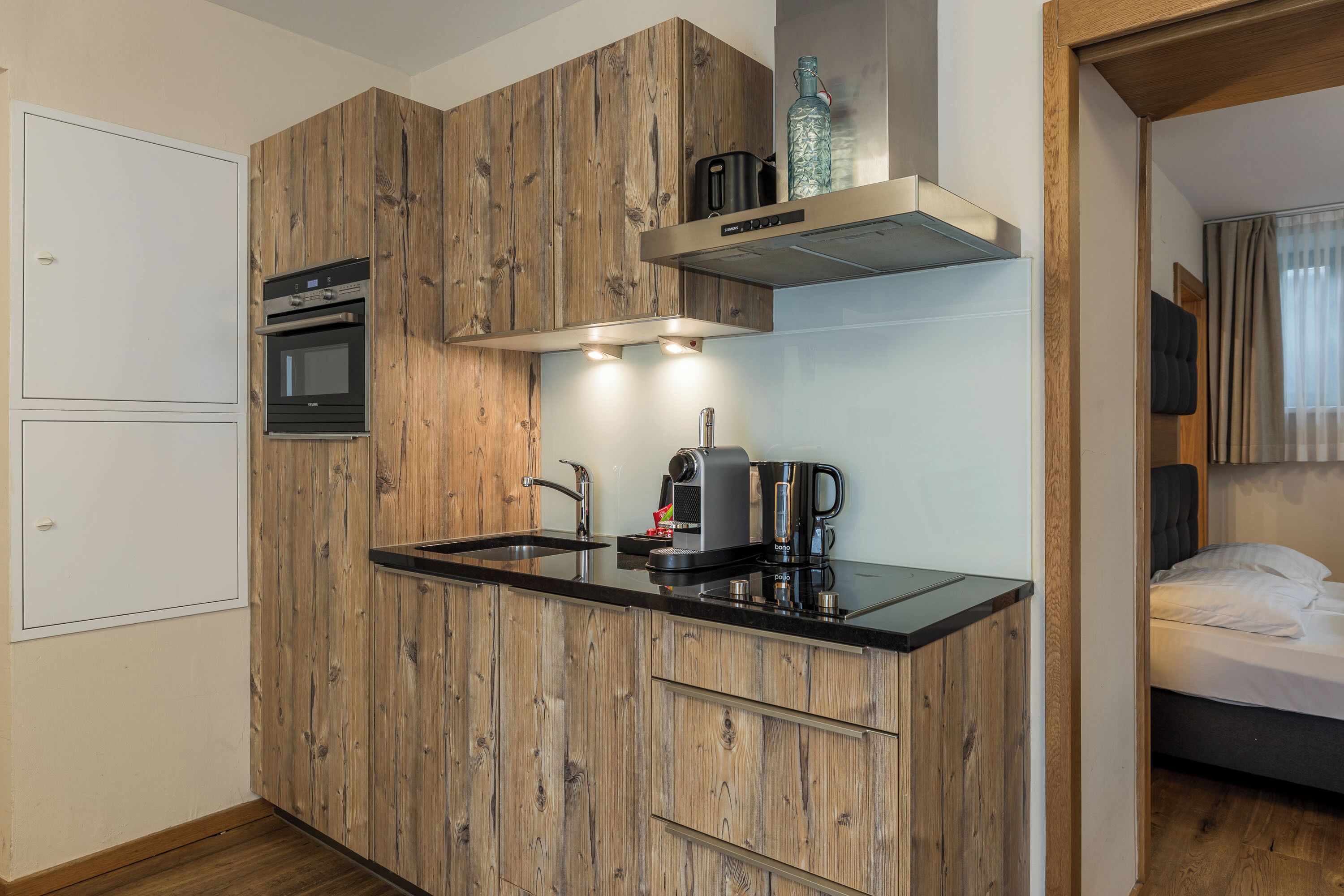 A compact kitchen with wooden cabinetry, a built-in oven, a coffee maker, and a microwave.