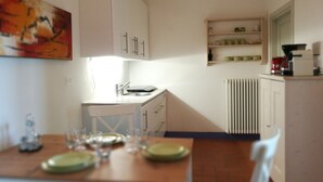 Een keuken met witte kastjes, een eettafel gedekt met borden en glazen, een koffiezetapparaat en een radiator.