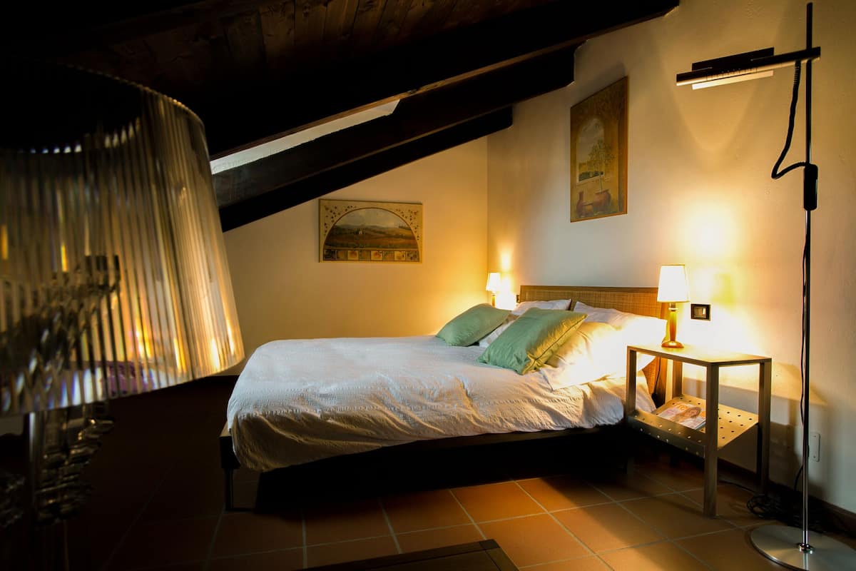 Een slaapkamer met een bed, twee bedlampen, een vloerlamp en een schilderij aan de muur.