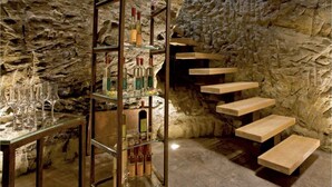 Une pièce aux murs de pierre, dotée d’un escalier en colimaçon et d’une vitrine en verre où sont exposées des bouteilles et des verres.