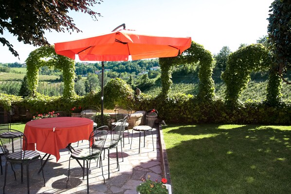 Une terrasse extérieure avec une table et des chaises en pierre, un parasol orange et une vue sur un vignoble.