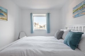 A bedroom with a bed, a window with curtains, and two paintings on the walls. - Spacious Flat, Sea Views & Private Parking, Fistral (Newquay)