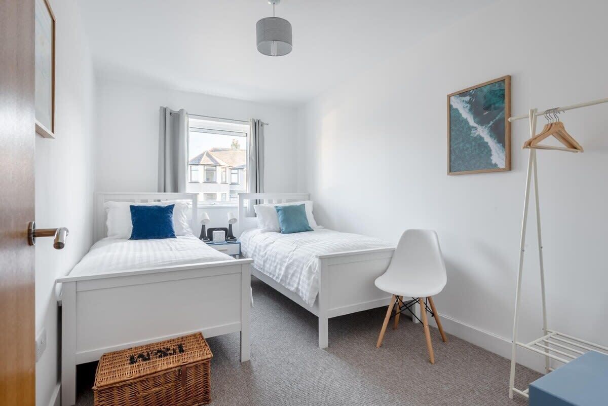 Une chambre avec deux lits, une chaise, un portant et une fenêtre avec des rideaux.