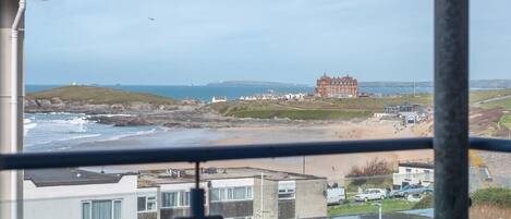 A balcony with a table and chairs, overlooking a beach and buildings.