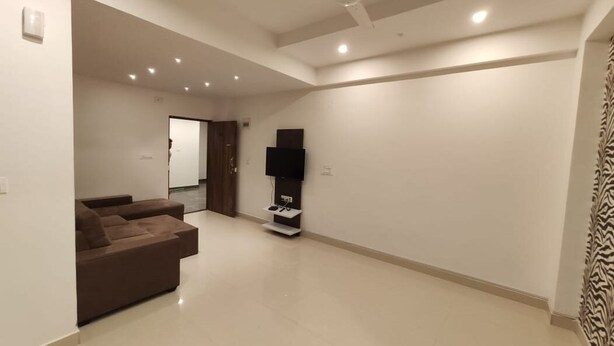 A spacious living room with a brown sofa, a ceiling fan, recessed lighting, and a flat-screen TV on a stand. - JUSTWALKIN ROOMS - Budgeted Rooms in Bangalore (Bengaluru)
