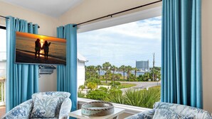 A room with a large window, two patterned armchairs, a small table, and a painting of two people on a beach. - Snowbird Special Jan Feb! 🌊Harbor View~Walk2Beach~2BR Beach Side-Harbor View (Destin)