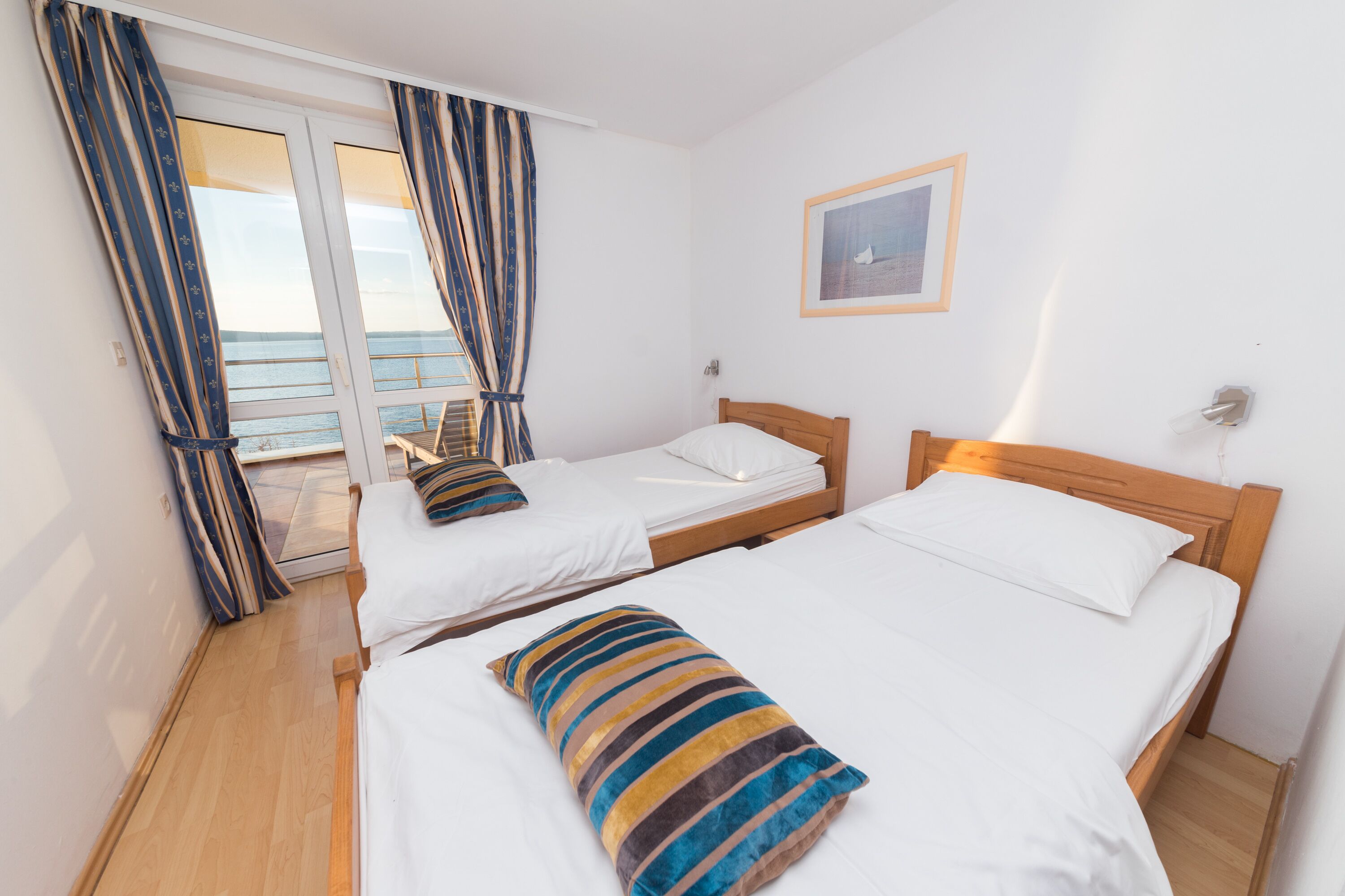 A hotel room with two beds, a wooden headboard, a large window with curtains, and a framed picture on the wall.