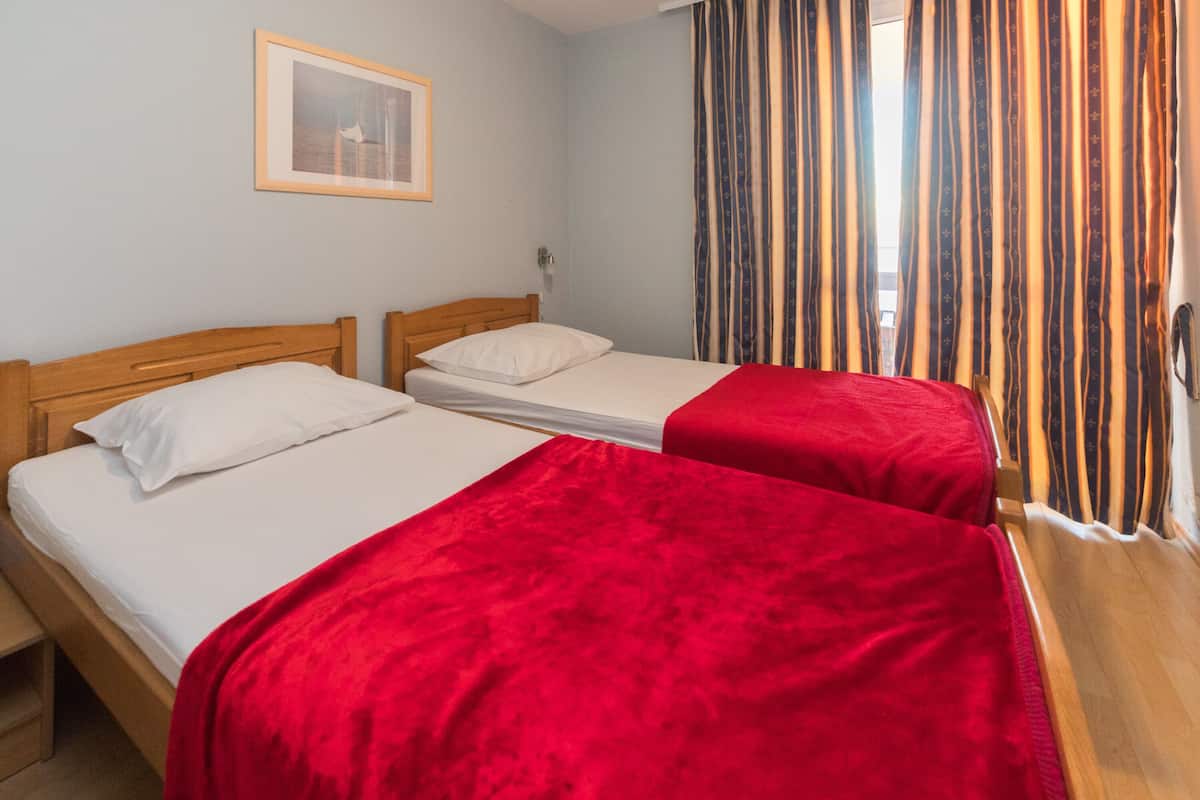 A room with two single beds, each with a wooden headboard and white bedding. There is a framed picture on the wall above the left bed.