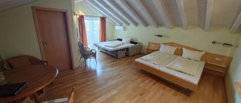 Una habitación con piso de madera, una cama, un sofá, una mesa de comedor y una silla.