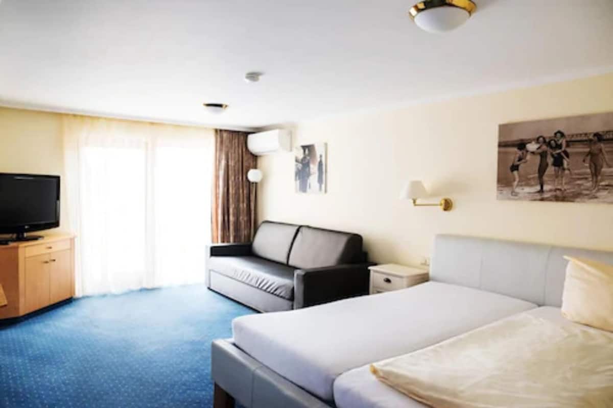 Een hotelkamer met een bed, een slaapbank, een televisie, een nachtkastje en een raam met gordijnen.