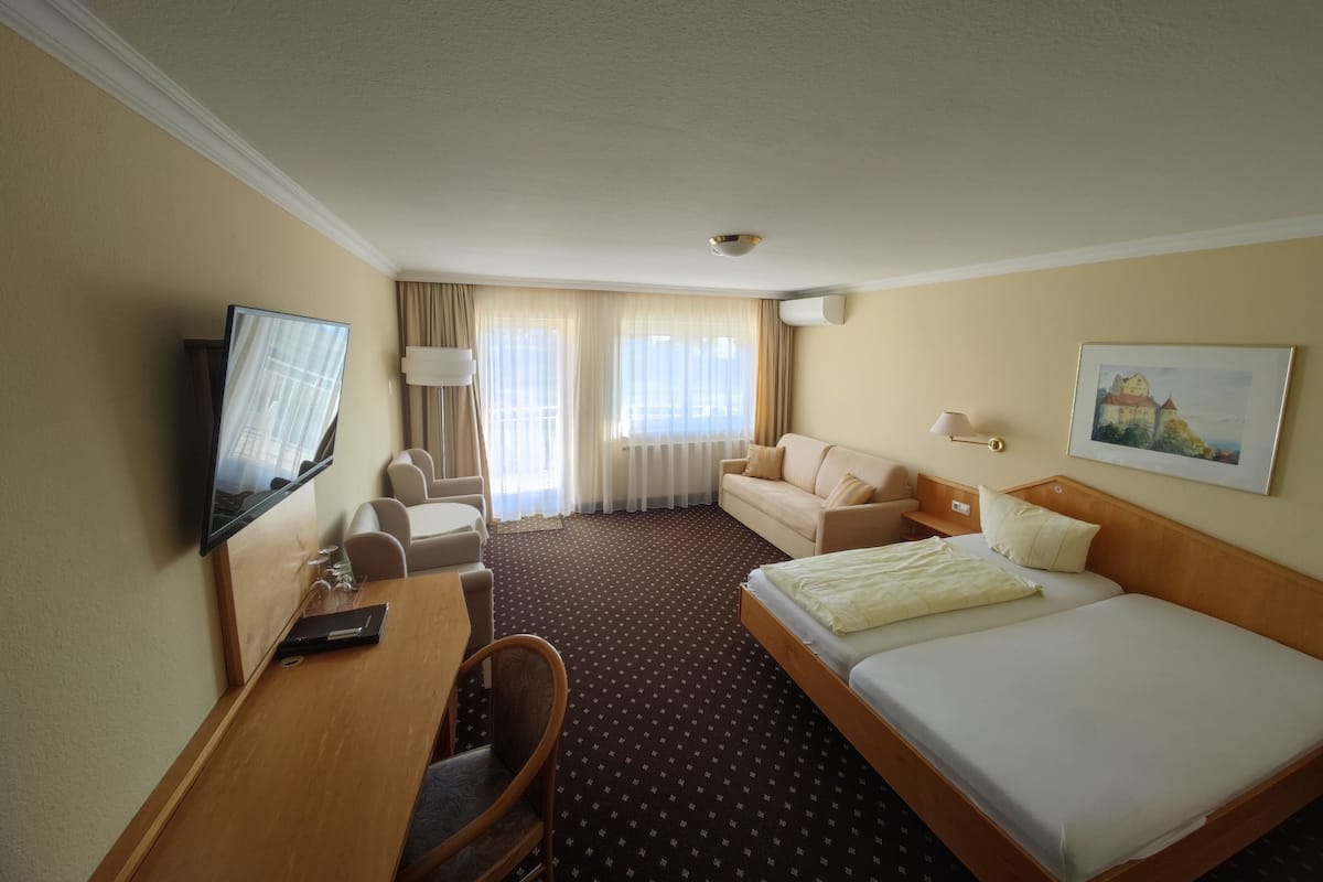 Een hotelkamer met een bed, een bureau met stoel, een bank, een televisie en een schilderij aan de muur.
