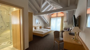 A hotel room with a bed, a desk, a chair, a TV, and a shower area. - Sporthotel  Schönblick (Meersburg)