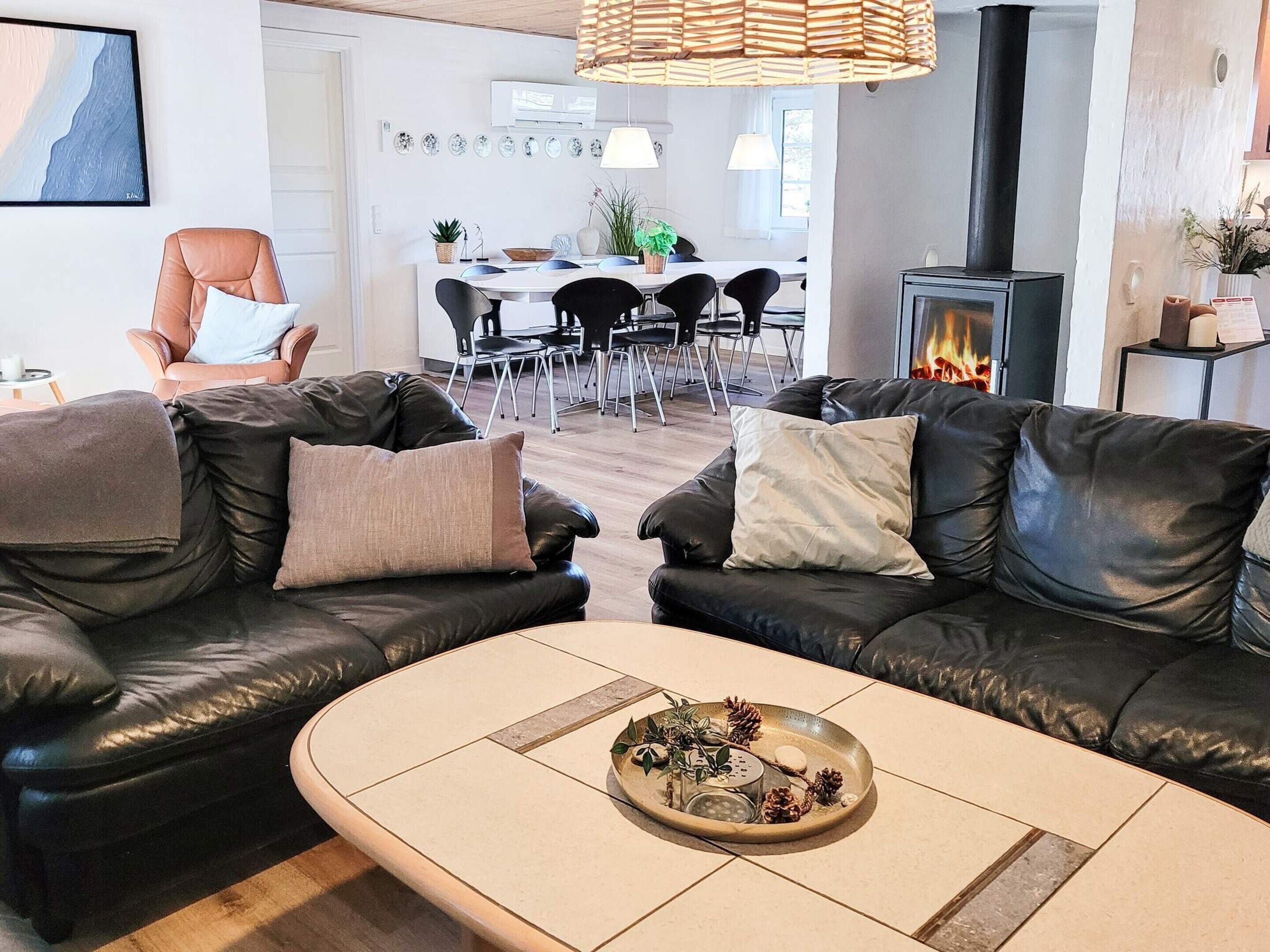 A modern living room with leather sofas, a coffee table with decorative items, a dining area in the background, and a fireplace.