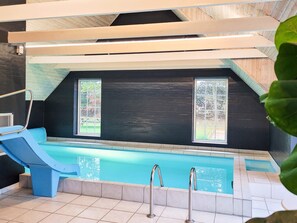 An indoor swimming pool with a blue slide, two windows, and a tiled floor. - 5 Star Holiday Home in Ulfborg (Ulfborg)