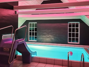 A pool area with a slide, two windows, and a ceiling with pink lighting.