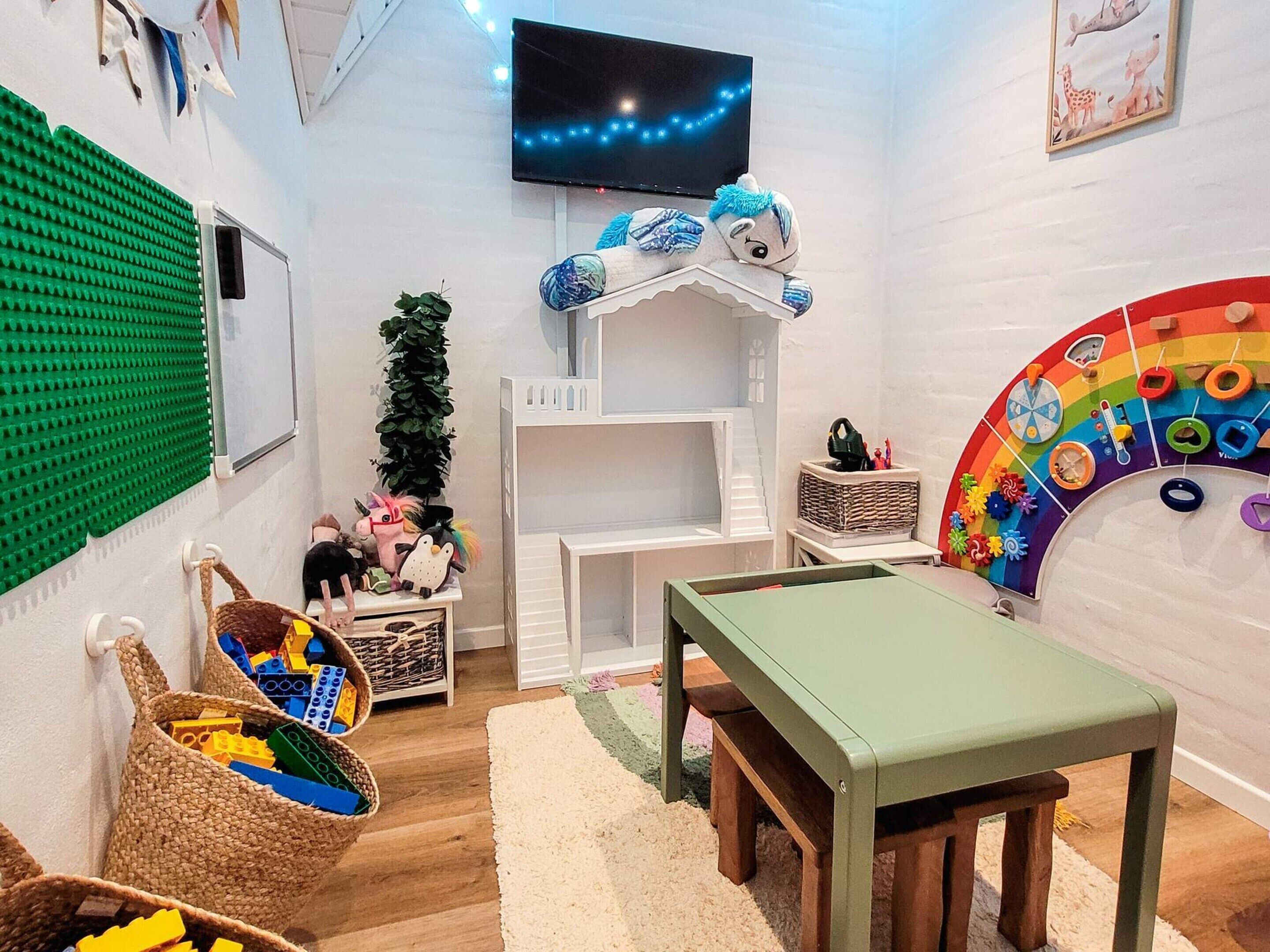 A children's playroom with a TV, play area, and a rainbow-colored wall decoration.