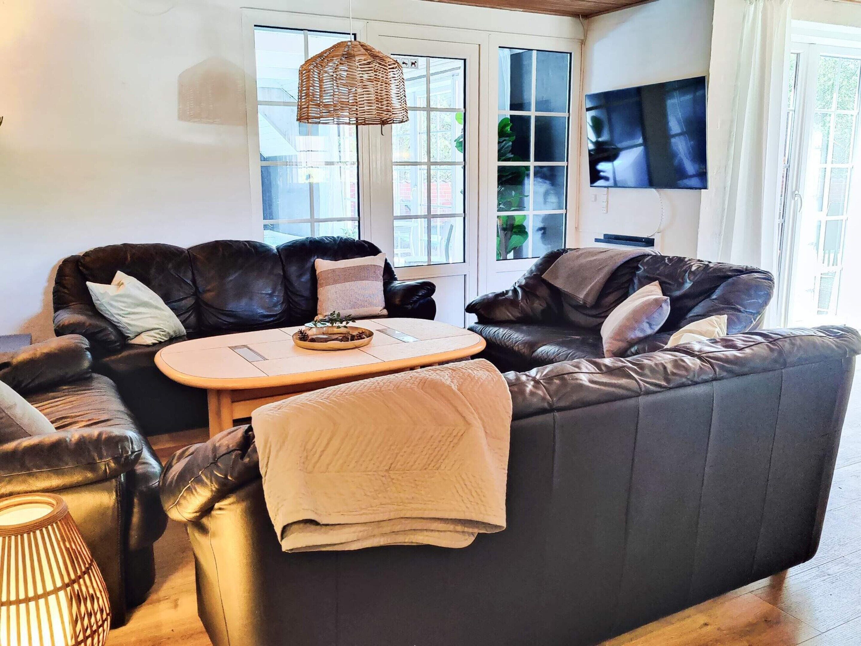 Ein Wohnzimmer mit einem dunkelbraunen Ledersofa, einem Holztisch und einer gewebten Pendelleuchte.