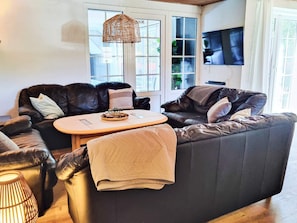 A living room with a dark leather sofa, a wooden coffee table, and a woven pendant light. - 5 Star Holiday Home in Ulfborg (Ulfborg)