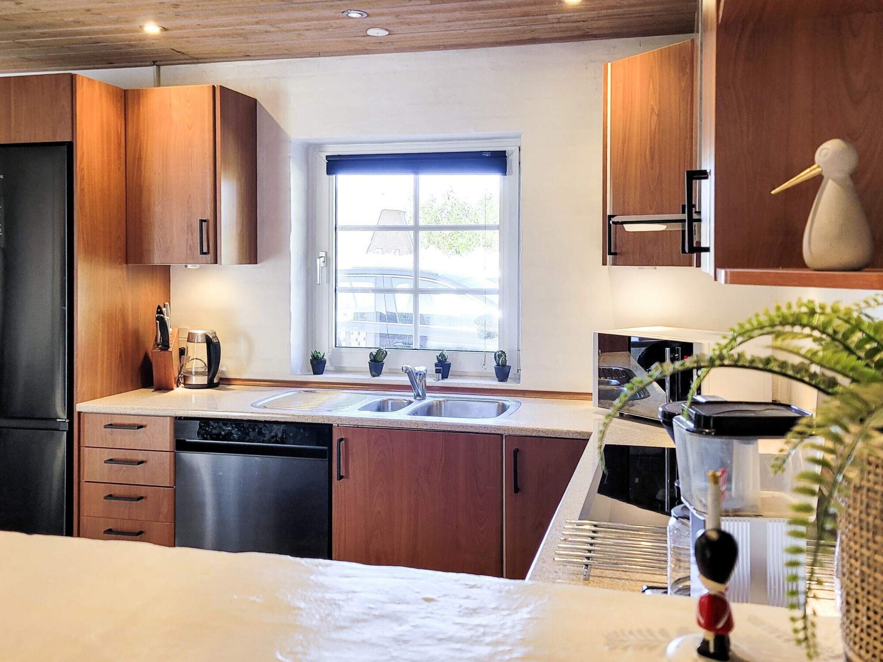 A modern kitchen with wooden cabinets, a double sink, and a window with a view of a building outside.