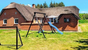 A brick house with a thatched roof, a swing set, and a slide in the yard.