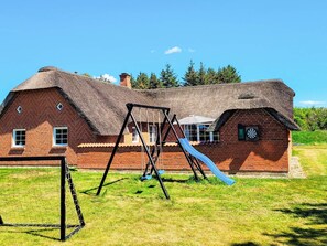 A brick house with a thatched roof, a swing set, and a slide in the yard. - 5 Star Holiday Home in Ulfborg (Ulfborg)