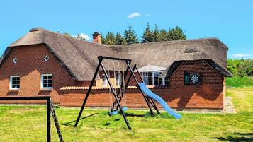 A brick house with a thatched roof, a swing set, and a slide in the yard.